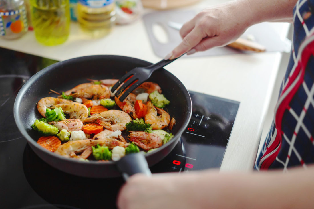 Manos cocinando en un sarten, mariscos con verduras